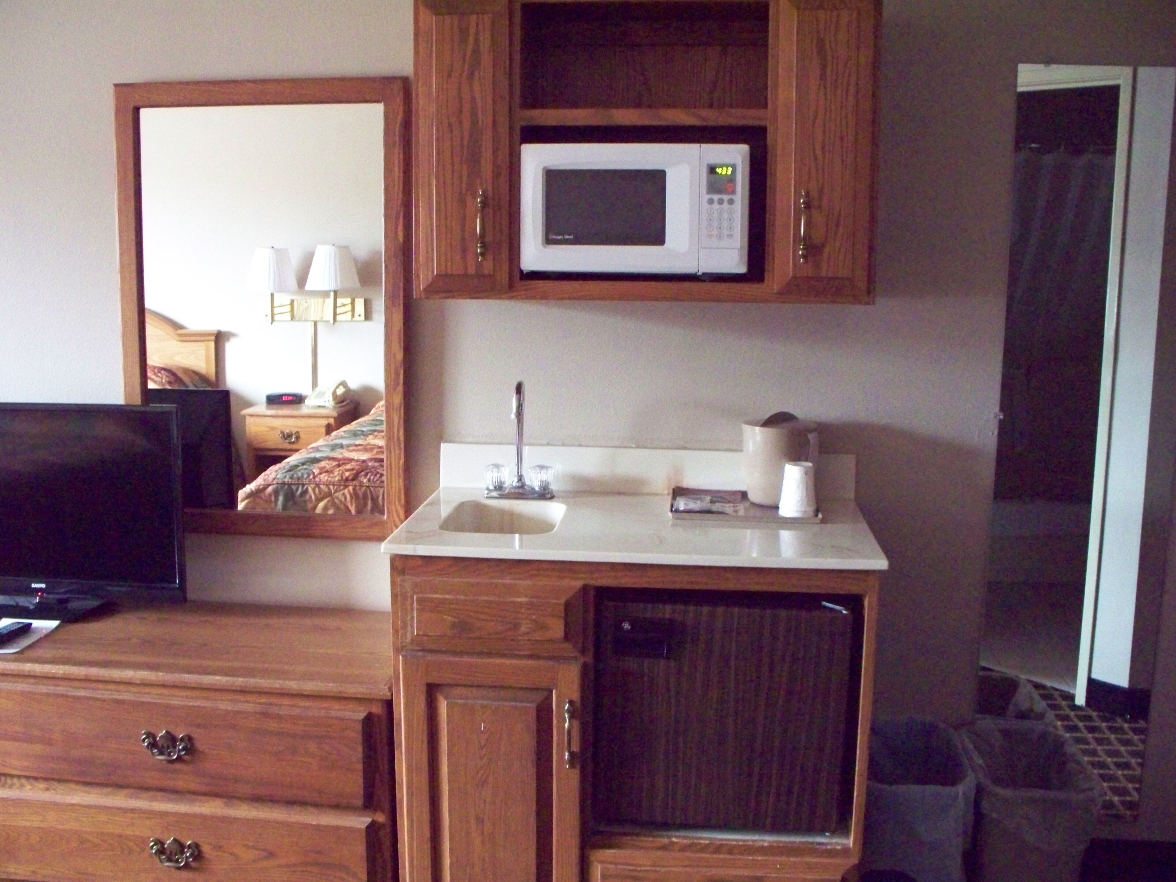 A hotel room with wooden cabinetry, a microwave, a sink, and a television.