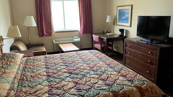 Habitación de hotel con una cama grande, un escritorio, una silla, un aparador, un televisor y una ventana con cortinas.