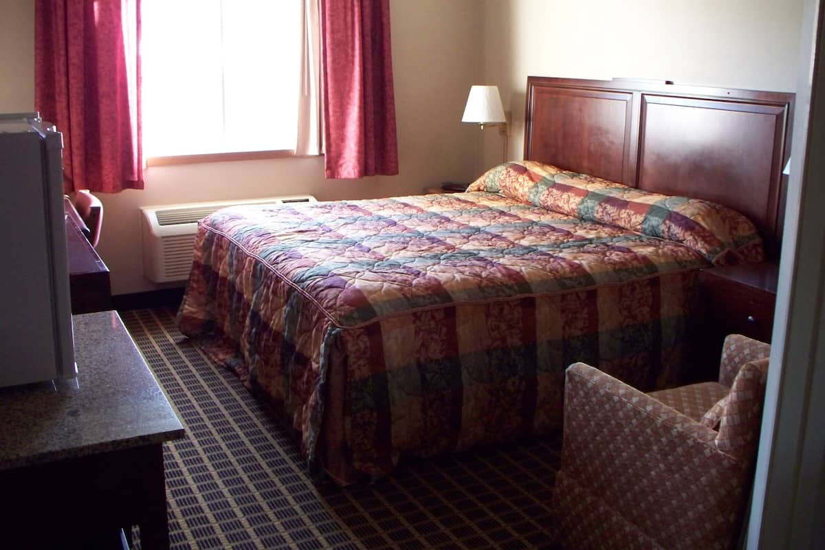 A hotel room with a bed, a desk, a chair, a lamp, and a window with curtains.