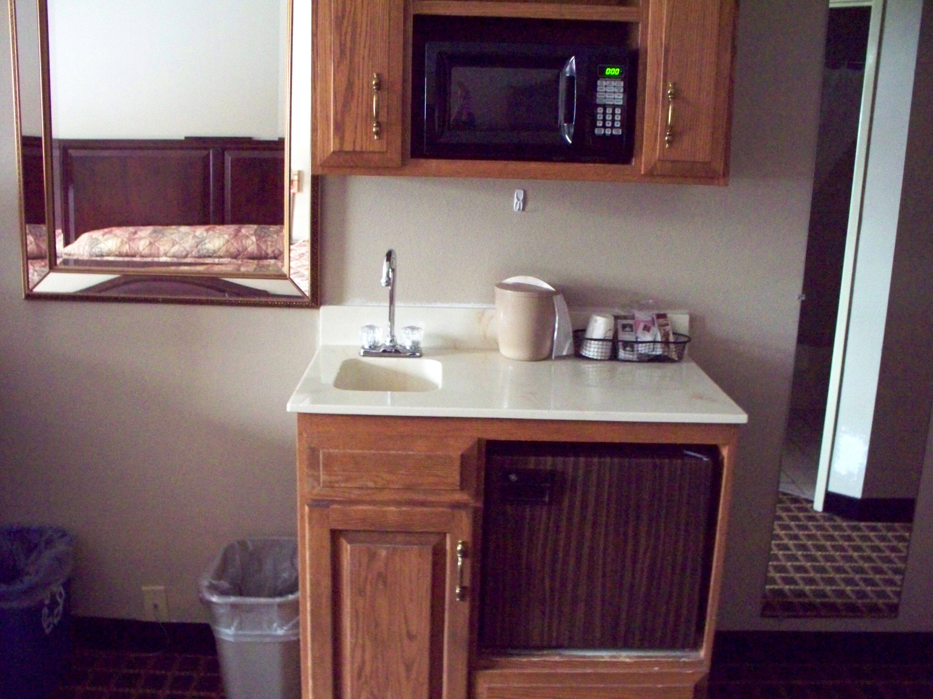 A bathroom with a sink, mirror, microwave, and toiletries.