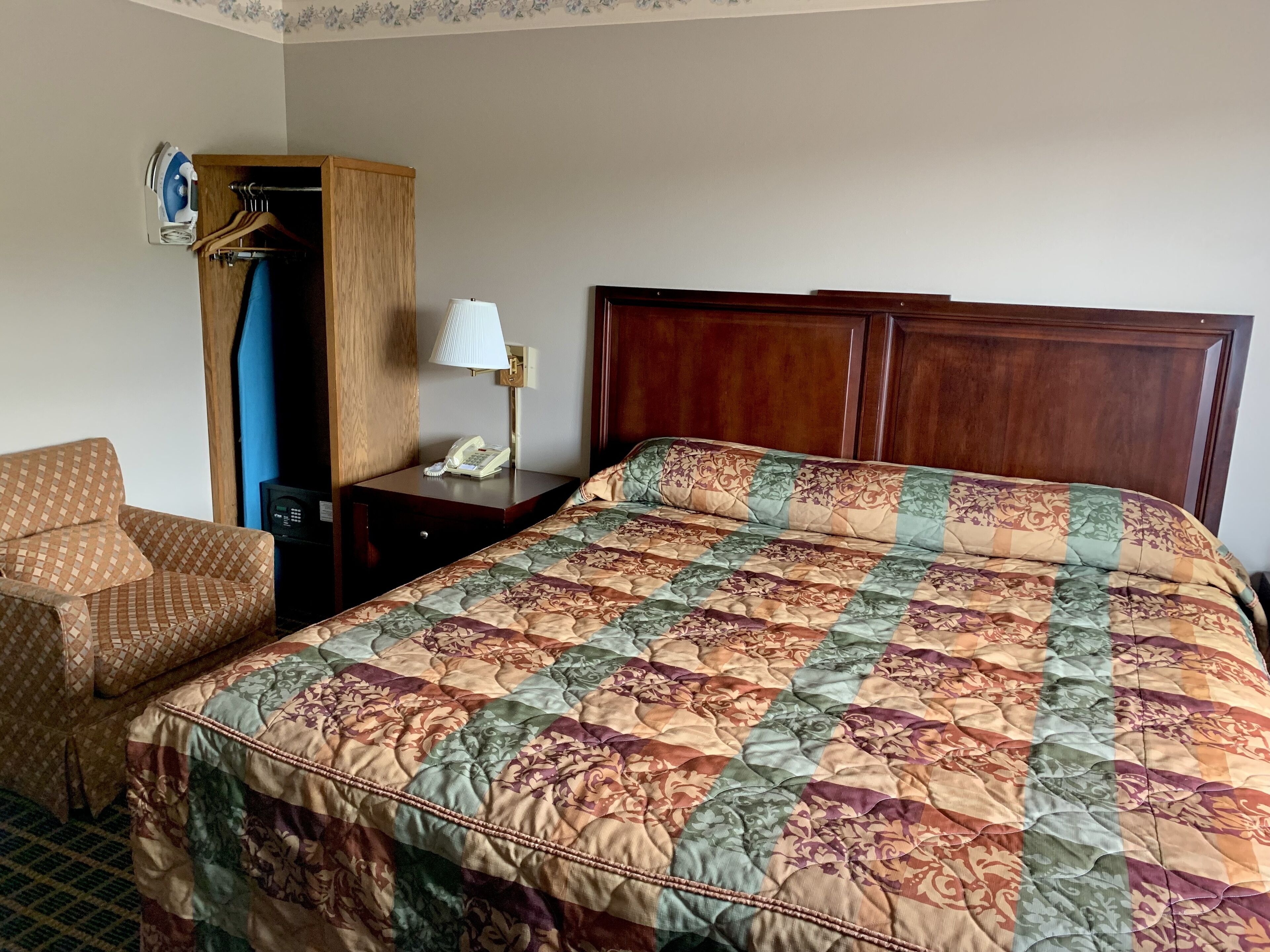 Een hotelkamer met een groot bed, een houten hoofdbord, een nachtkastje met een lamp, een telefoon en een kledingkast met daarin hangruimte.