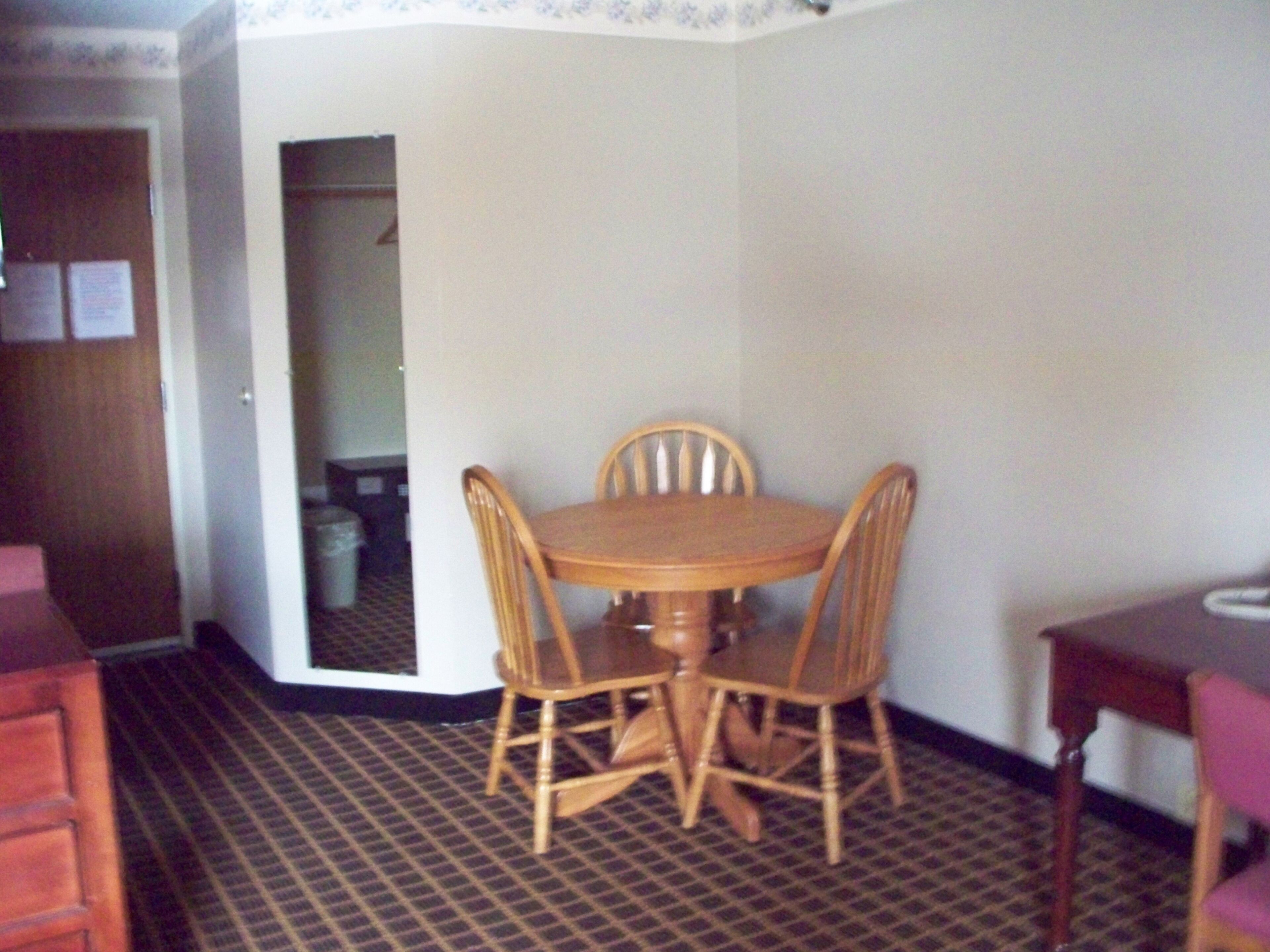 Un comedor con una mesa redonda de madera y cuatro sillas. Hay una puerta que da a otra habitación.