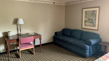 Une chambre d’hôtel avec un bureau en bois, une chaise rose, un canapé bleu, une moquette à motifs et un tableau encadré au mur.
