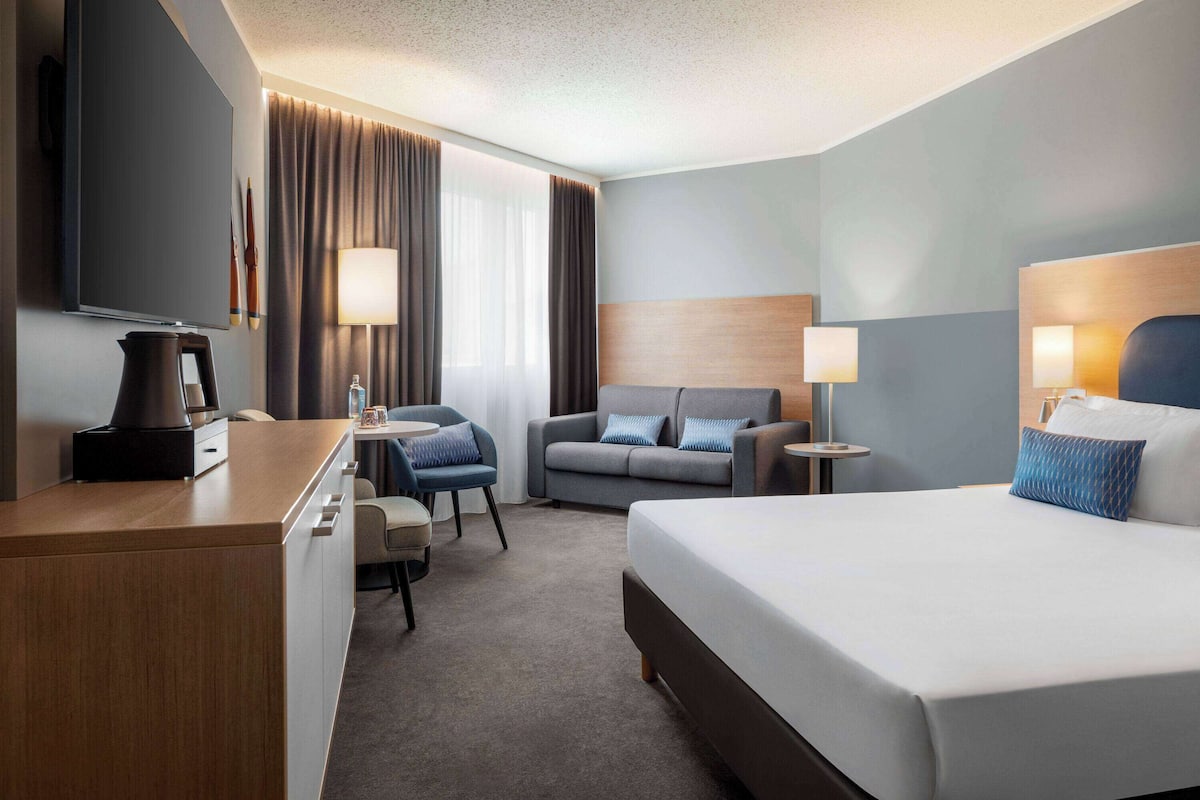 A hotel room with a bed, a desk, a sofa, a TV, and a lamp.