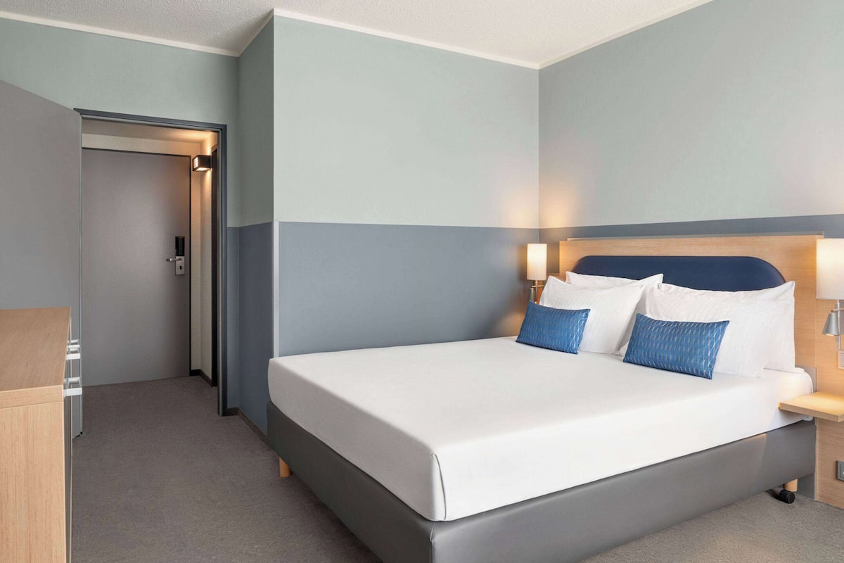A modern hotel room with a large bed, bedside lamps, and a wooden nightstand.