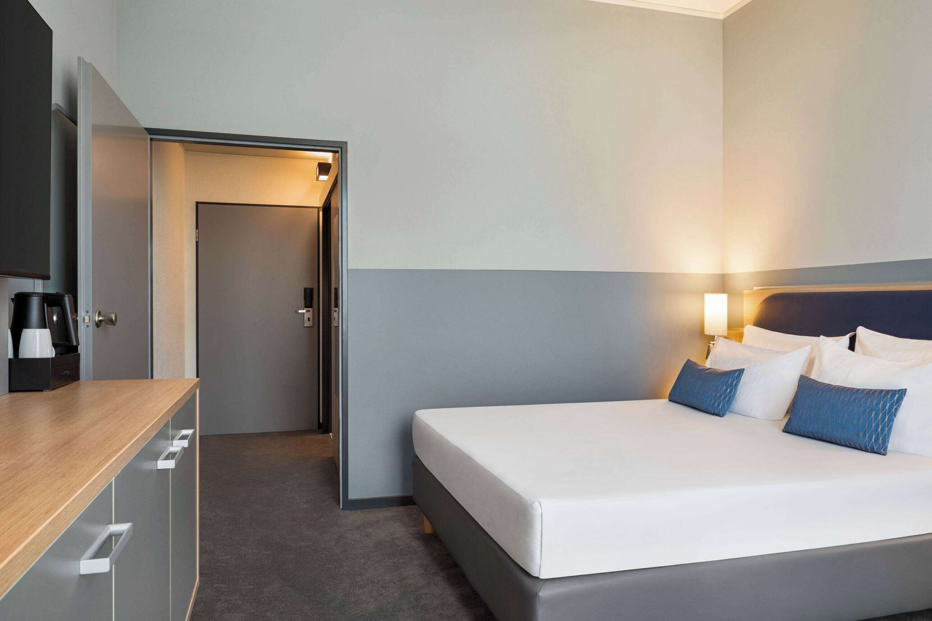 A hotel room with a bed, bedside table, and a door leading to another room.