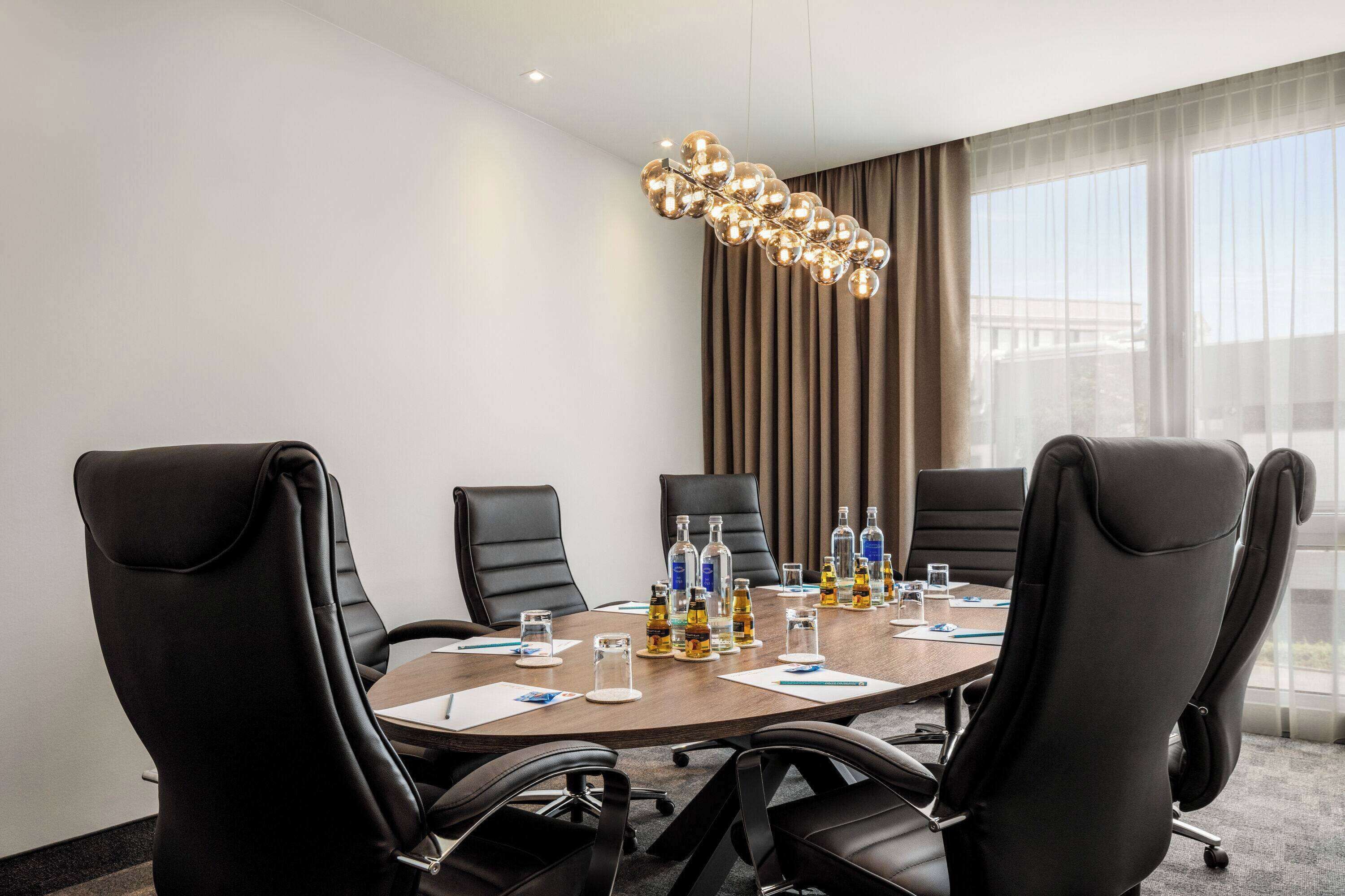 A conference room with a round table, black leather chairs, and a modern chandelier.