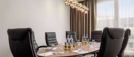 A conference room with a round table, black leather chairs, and a modern chandelier.
