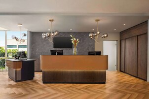 Un área de recepción moderna con suelo de parqué en espiga, una recepción central con un jarrón de flores y un televisor de pantalla plana grande en la pared.