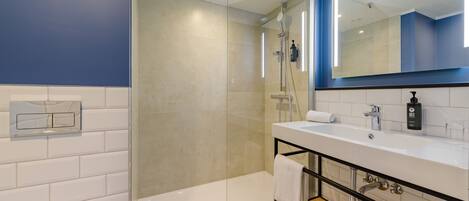 Un baño moderno con ducha envuelta en vidrio, un lavabo blanco con estructura negra y un espejo grande sobre el lavabo.