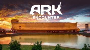 A large ark-like structure with a reflection in a body of water, set against a sunset sky.