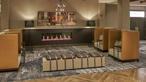 A lobby with sofas, a fireplace, and artwork on the wall. - Hilton Cincinnati Airport (Florence)