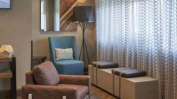A modern living room with a blue armchair, a brown armchair, a sofa, a floor lamp, and a patterned curtain.