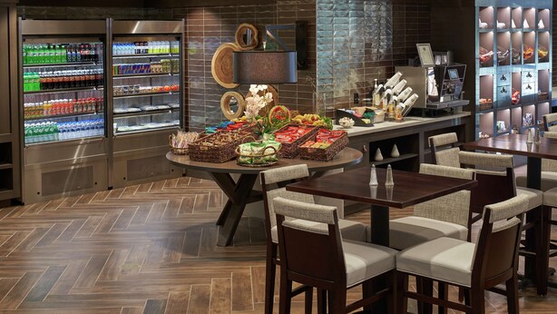 A hotel lobby with a reception area, a coffee station, and a buffet with various food items. - Hilton Cincinnati Airport (Florence)