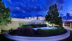 A hotel with a swimming pool, landscaped garden, and a view of the sky. - Hilton Cincinnati Airport (Florence)