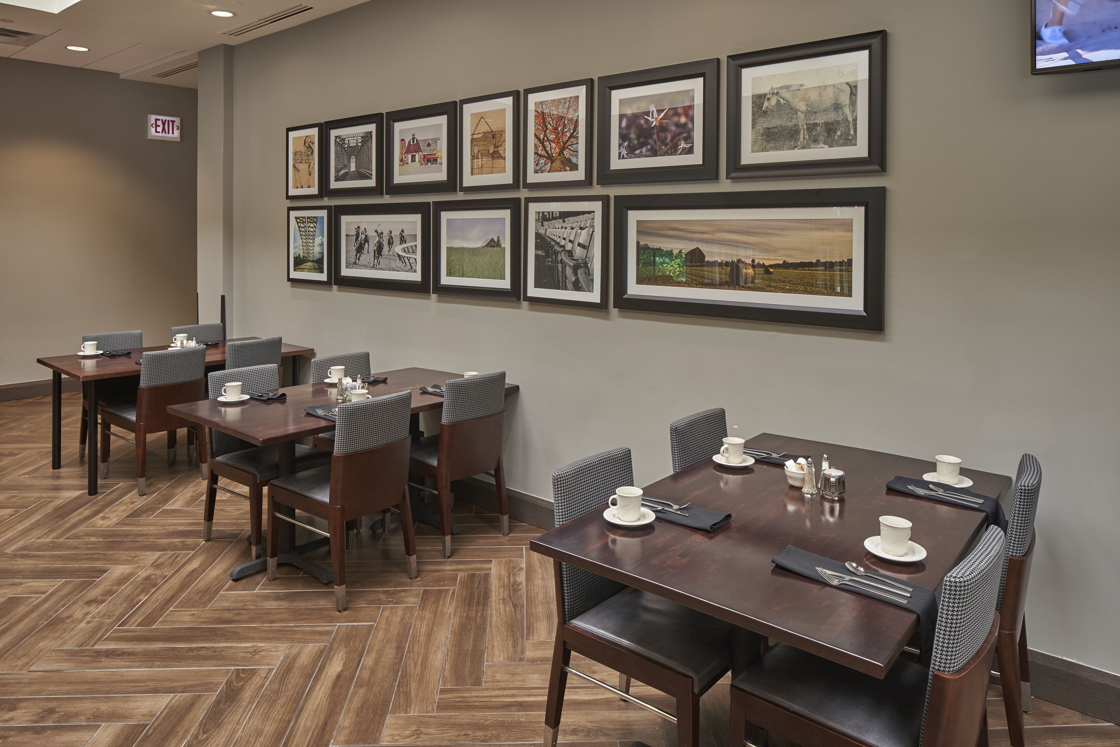 A conference room with multiple tables and chairs, framed pictures on the wall, and an exit sign.