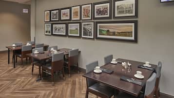A conference room with multiple tables and chairs, framed pictures on the wall, and an exit sign.