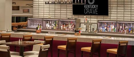 Un espace bar agrémenté d’une enseigne sur le thème du Kentucky, de plusieurs distributeurs de boissons alcoolisées et de différents types de sièges.