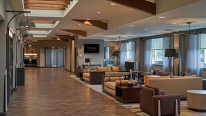 A spacious hotel lobby with a long corridor, comfortable seating areas, and large windows offering views of the outside. - Hilton Cincinnati Airport (Florence)