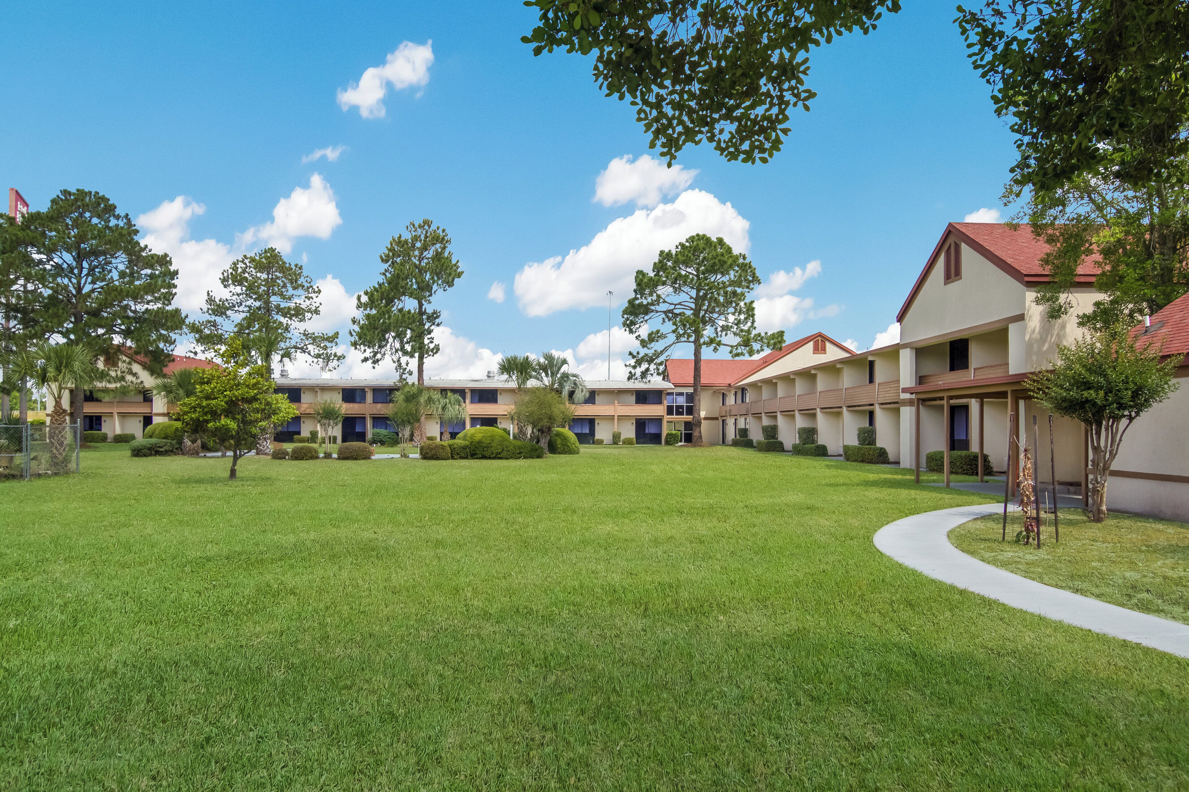 A courtyard with a lawn, trees, and a row of buildings with a red roof.