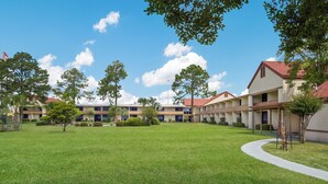 A courtyard with a lawn, trees, and a row of buildings with a red roof. - Red Roof Inn & Suites Brunswick I-95 (Brunswick)