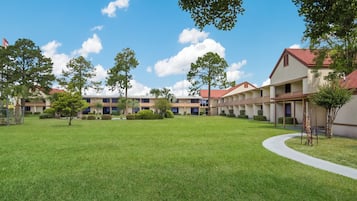 A courtyard with a lawn, trees, and a row of buildings with a red roof.
