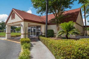 Standalone building with a covered entrance, surrounded by a manicured lawn and a palm tree.