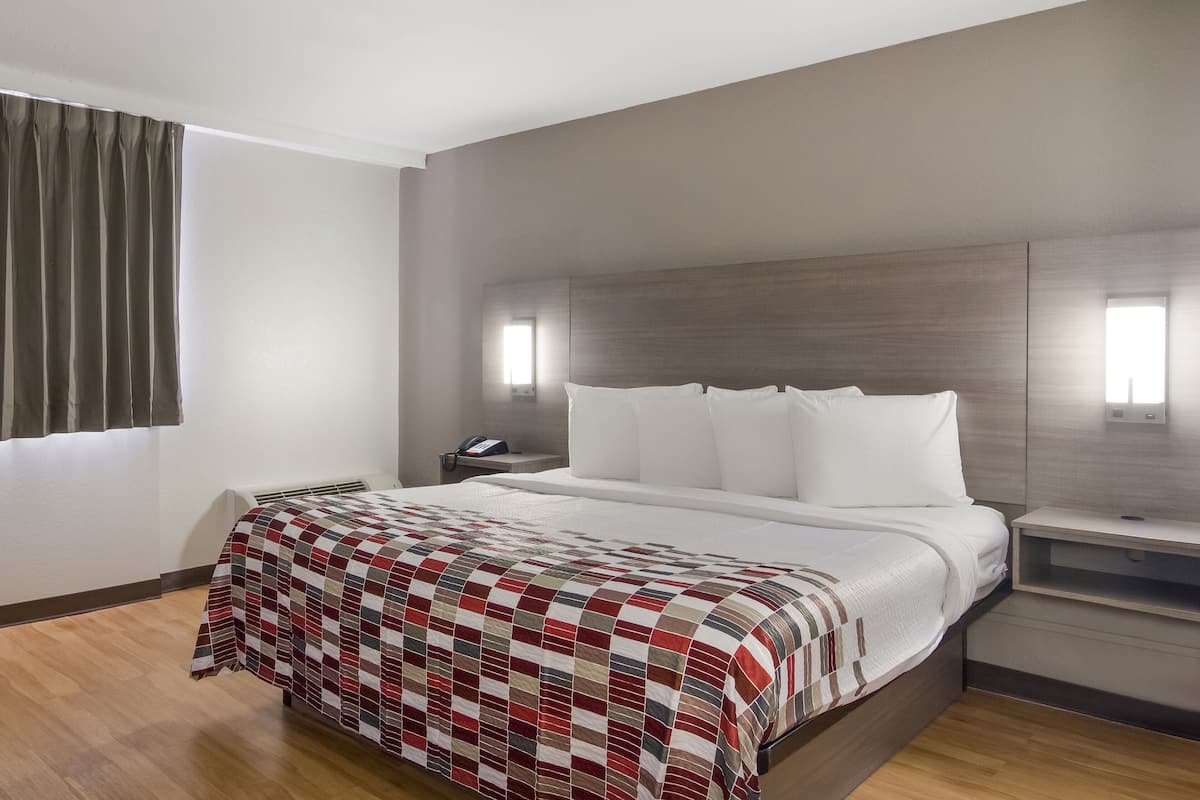 Ein Hotelzimmer mit einem großen Bett, einem Nachttisch und einem Fenster mit Vorhängen.