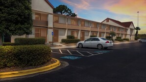 Ein Hotel mit Parkplatz, einem weißen Auto und einem blauen Parkplatzschild für Menschen mit Behinderung.
