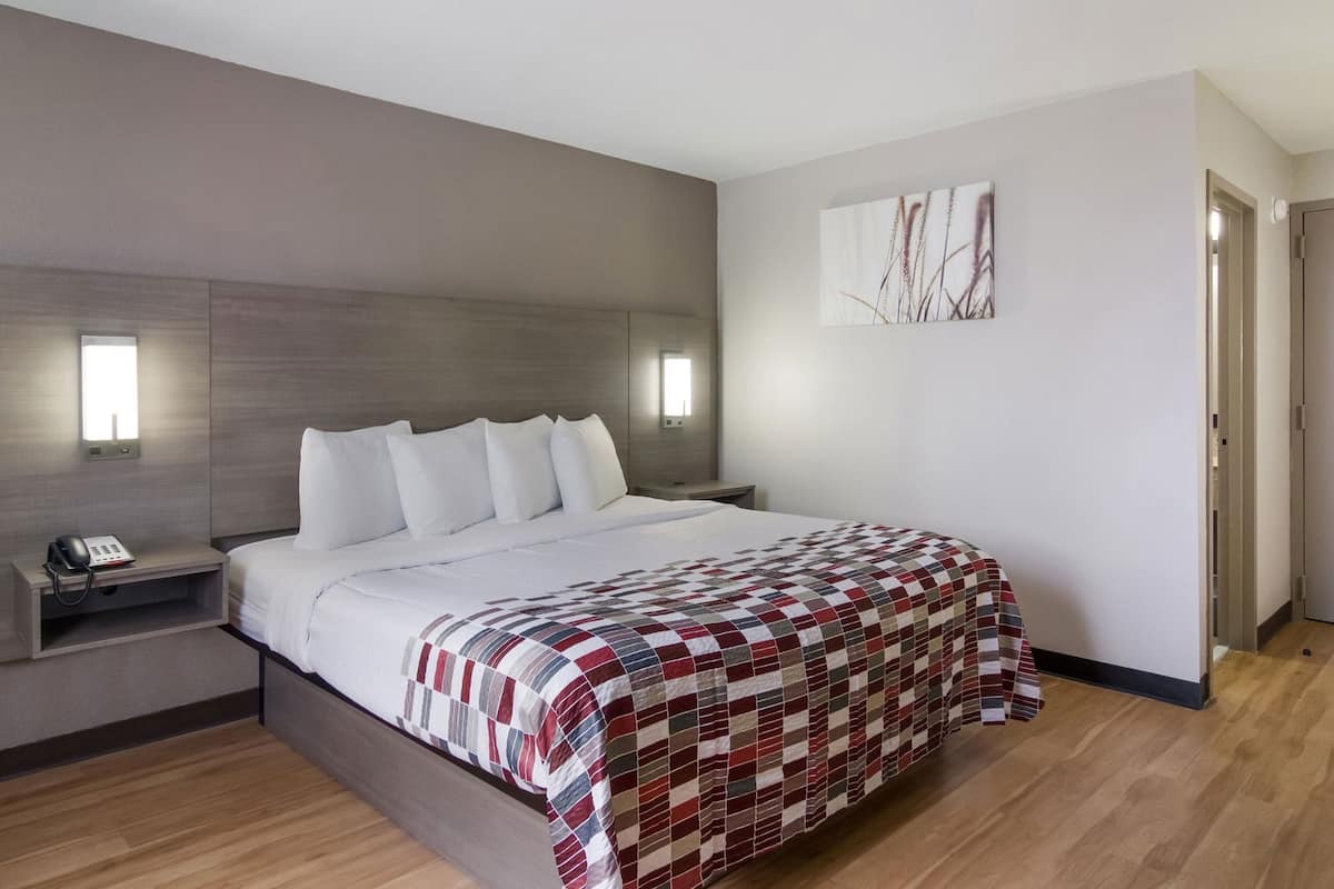 Ein modernes Hotelzimmer mit einem großen Bett, einem Nachttischtelefon, einer Wandleuchte und einem Gemälde.
