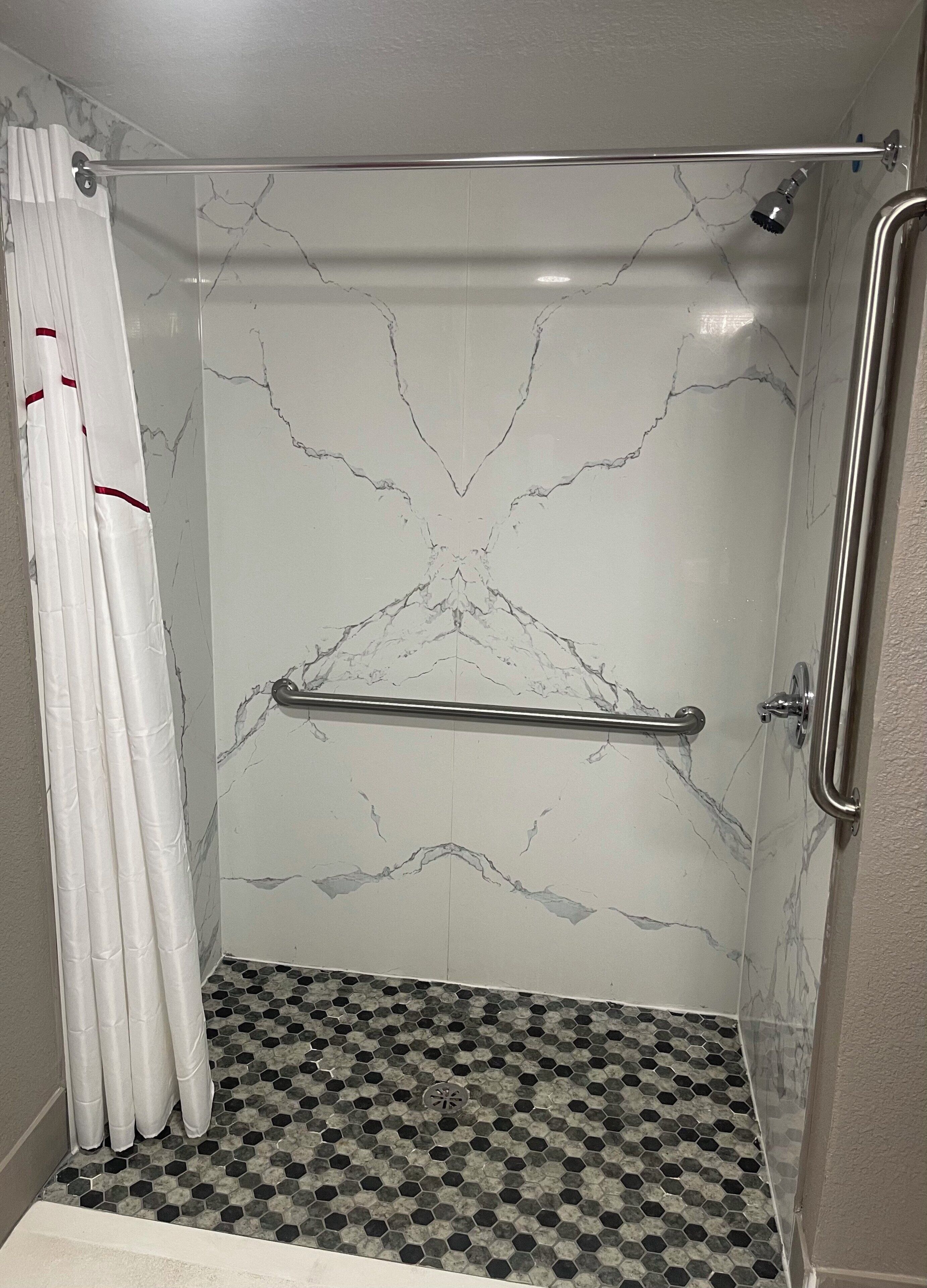 Eine Dusche mit weißer Marmorwand, einer Haltestange aus Metall und einem Boden mit sechseckigen Fliesen.