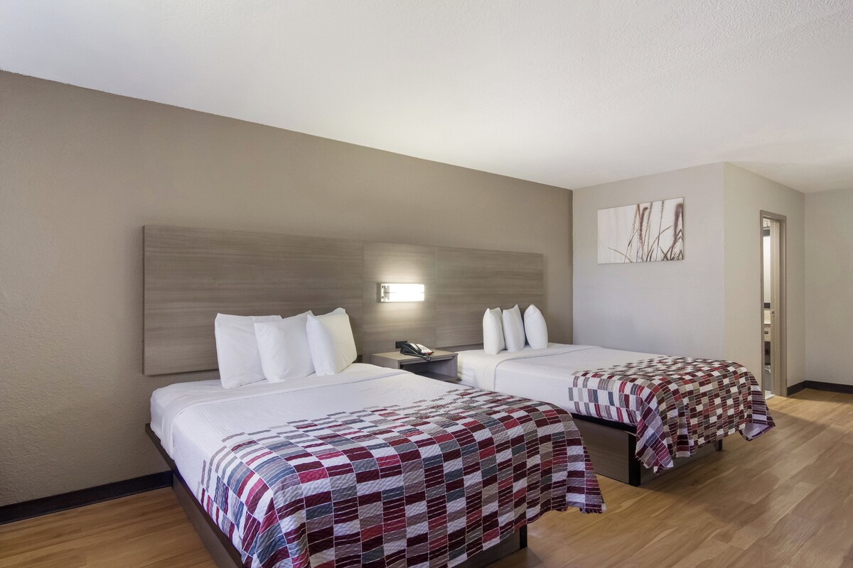 Habitación de hotel con dos camas, una mesita de noche, un teléfono y un cuadro en la pared.