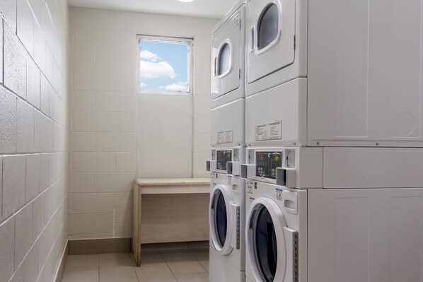 A laundry room with stacked washing machines, a small window, and a wooden bench. - Red Roof Inn & Suites Brunswick I-95 (Brunswick)