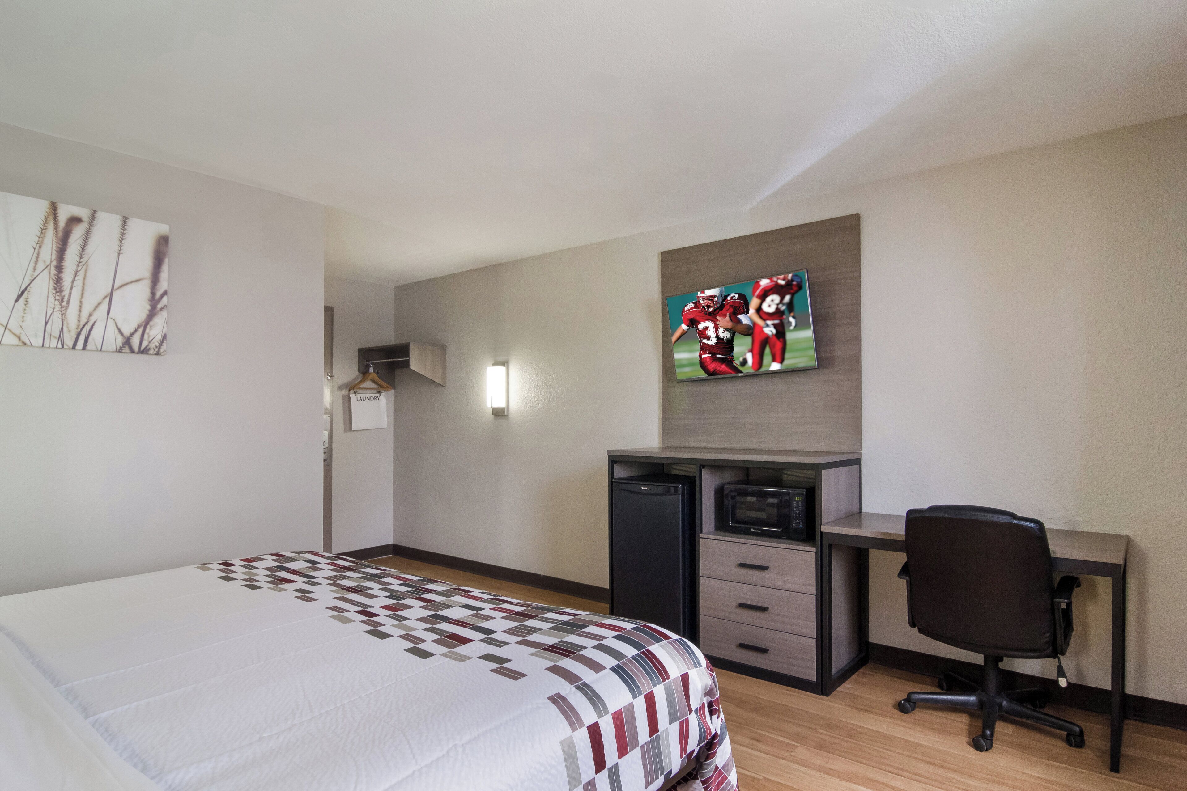 A hotel room with a bed, a desk, a television, and a refrigerator.