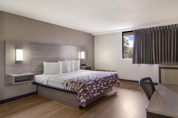 Relax in a serene space with a large bed, bedside table, and desk, perfect for work or rest.