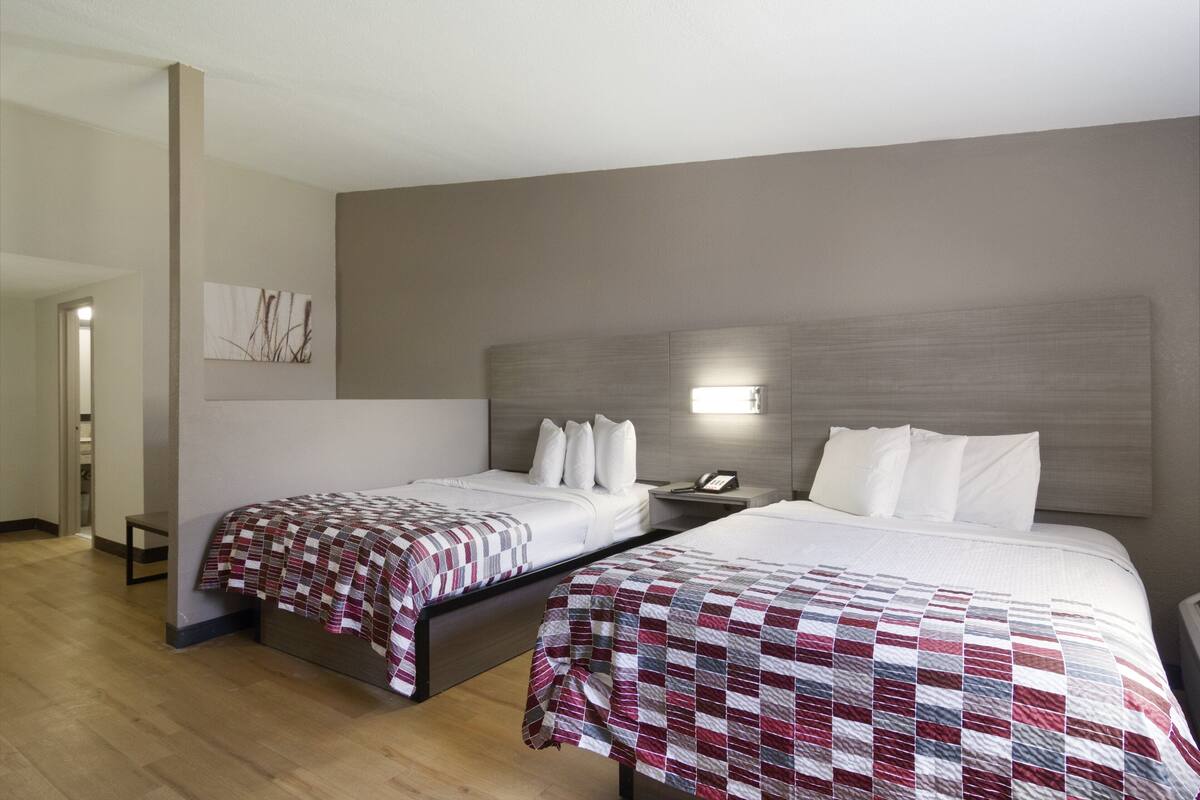 Ein Hotelzimmer mit zwei Betten, jedes mit einer anderen Musterdecke, einem Nachttisch mit Lampe und einem an der Wand hängenden Kunstwerk.