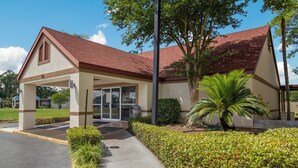 A building with a red roof, a covered entrance, and a well-maintained garden with a palm tree. - Red Roof Inn & Suites Brunswick I-95 (Brunswick)