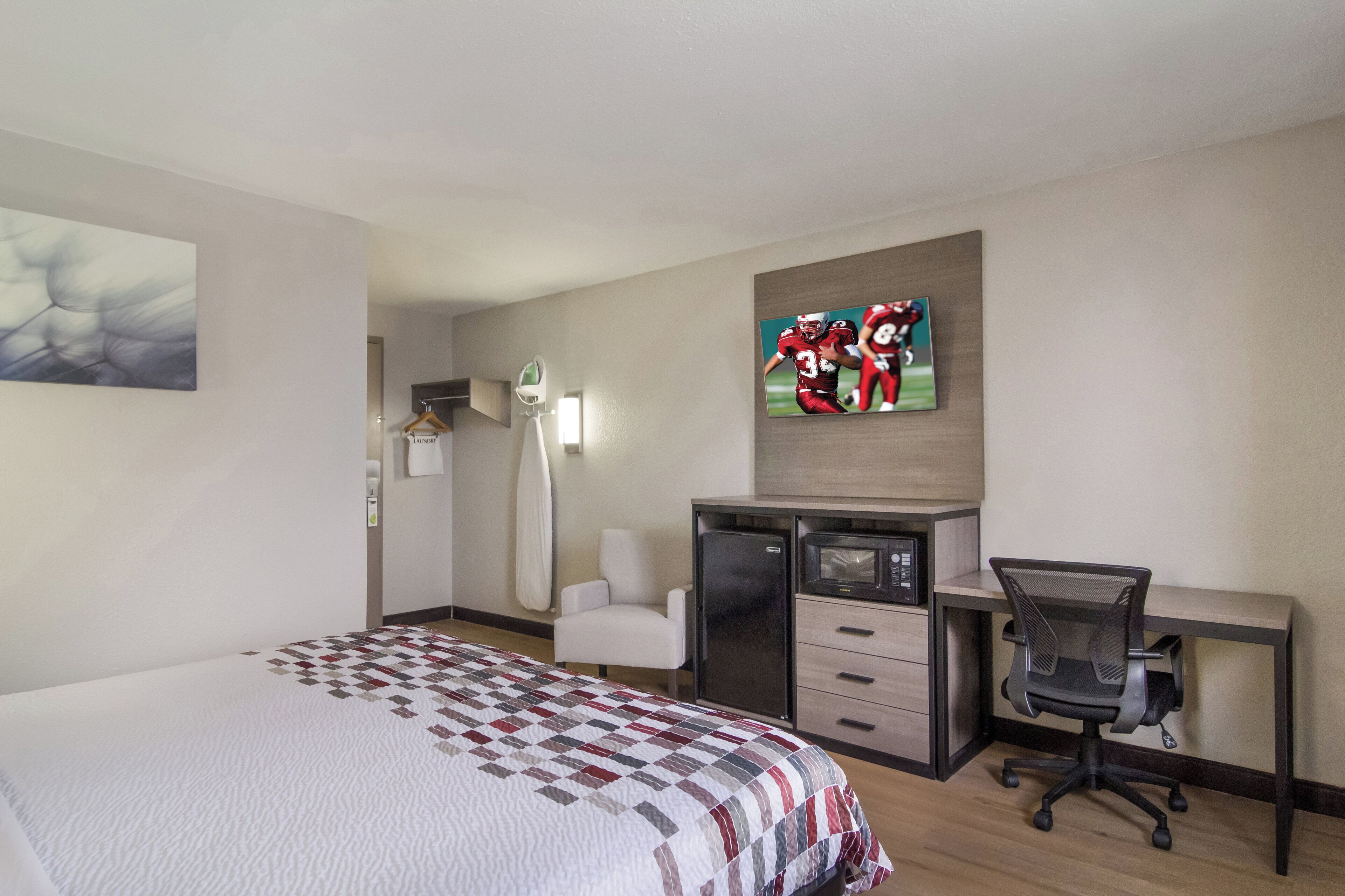 A hotel room with a bed, a desk, a chair, a television, and a wardrobe.