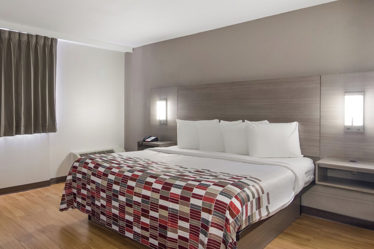 Habitación de hotel con cama, mesita de noche y ventana con cortinas.