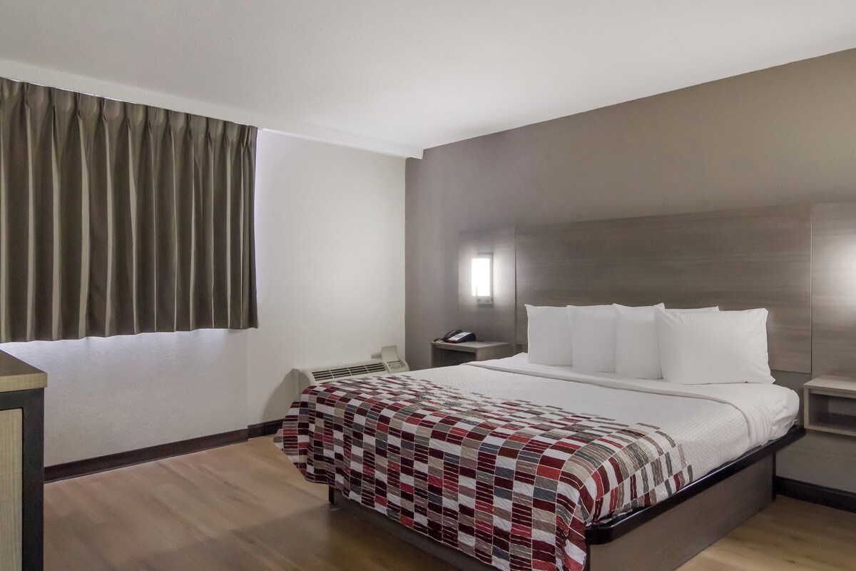 Una habitación de hotel con cama, mesita de noche, teléfono y ventana con cortinas.
