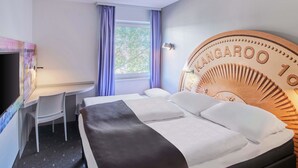Una habitación de hotel con una cama, un escritorio, una silla y un televisor montado en la pared.