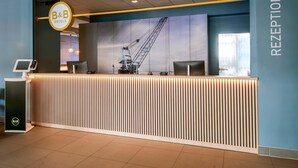 Un comptoir d’accueil avec une enseigne B&B Hotels, un espace de réception et une grande fenêtre donnant sur une grue.
