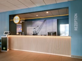 A reception desk with a B&B Hotels sign, a reception area, and a large window with a crane view.