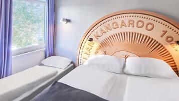 A hotel room with two single beds, a large wooden headboard with 'LANK KANGAROO 10' engraved, a window with curtains, and a wall-mounted lamp.