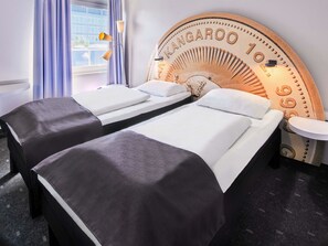 Habitación de hotel con dos camas, un cabecero grande con temática de canguro, una mesita redonda y una ventana con cortinas.