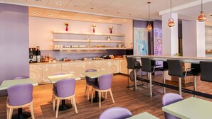 Un café moderno con sillas y mesas moradas, una zona de bar y estantes decorativos con flores.
