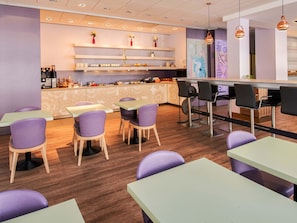 Una cafeteria moderna amb cadires i taules morades, una zona de bar i prestatges decoratius amb flors.