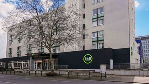 Un hôtel-chambre d’hôtes moderne, avec un logo bien visible sur la façade, de grandes fenêtres et un arbre devant l’entrée.