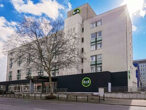 Un hotel tipo B&B moderno con un llamativo logotipo de B&B en la fachada, ventanas amplias y un árbol en primer plano.