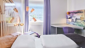 Une chambre d’hôtel avec un lit, un bureau, une chaise et une fenêtre avec des rideaux.